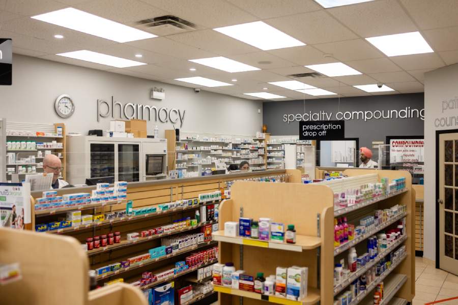 Interior of a well-organized pharmacy with shelves stocked with various medications and products, with several pharmacists visible behind the counter.